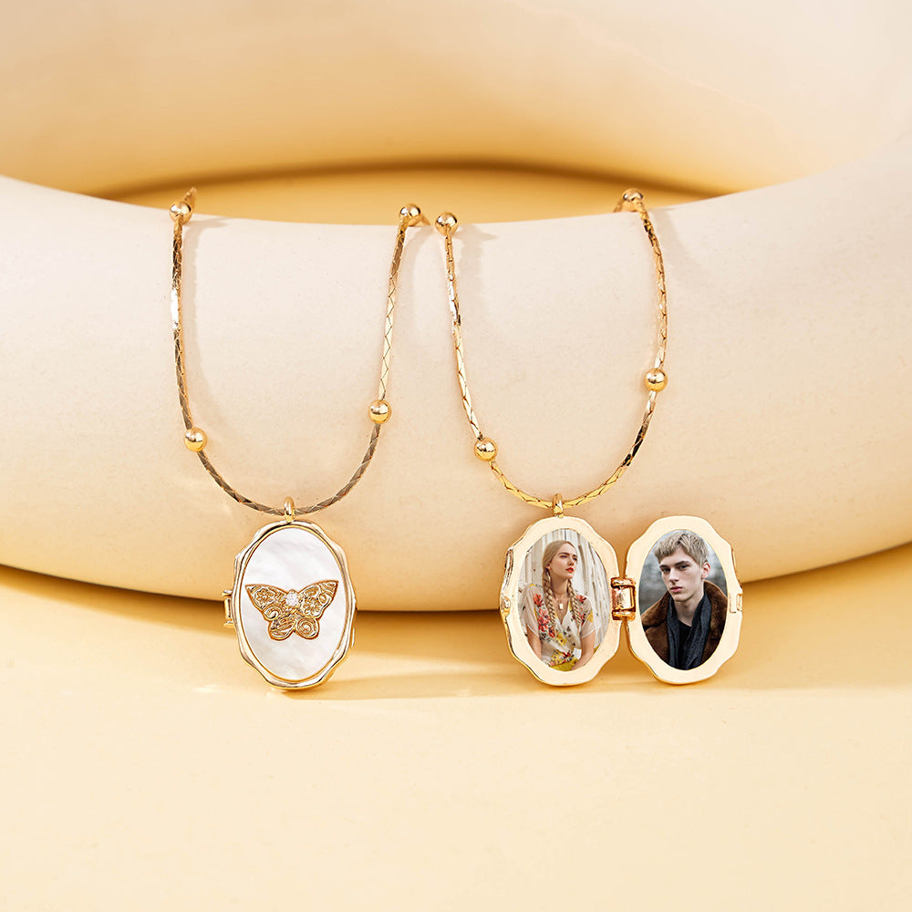 Two oval gold brass photo lockets with natural shell butterfly details placed on beige display bracket