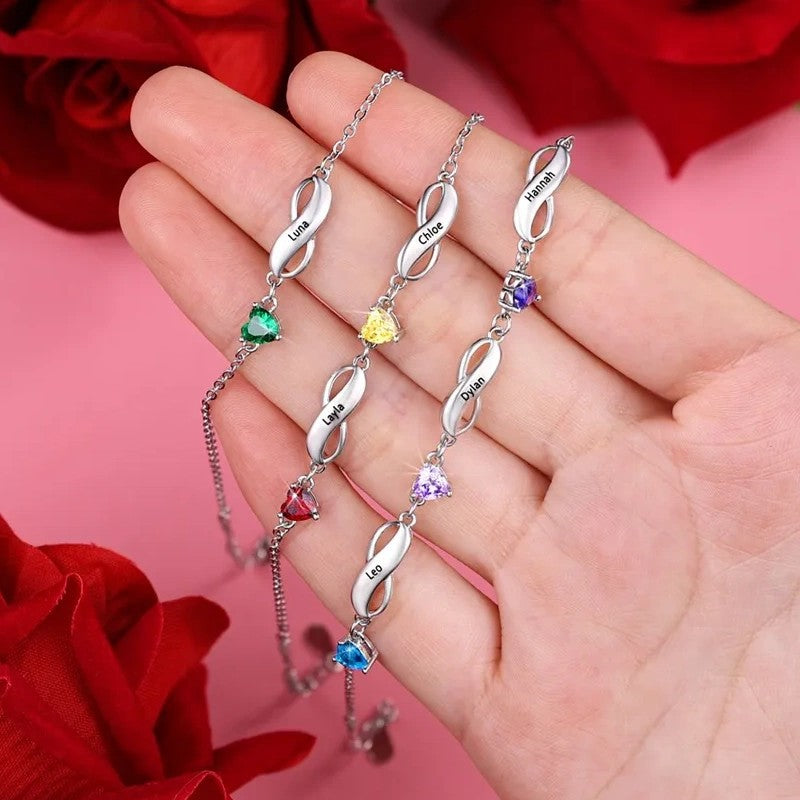 Silver brass infinity birthstone bracelet with multi-colored heart zircon displayed laid flat in human palm with red rose backdrop