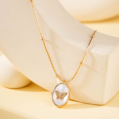 Studio shot of gold plated brass oval locket embedded with natural shell butterfly paired with delicate beaded cable chain