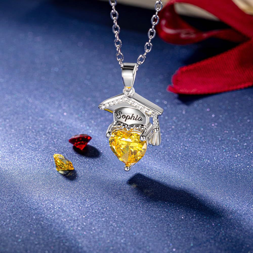 Silver brass engraved graduation cap necklace with yellow heart zircon shot on dark fabric background